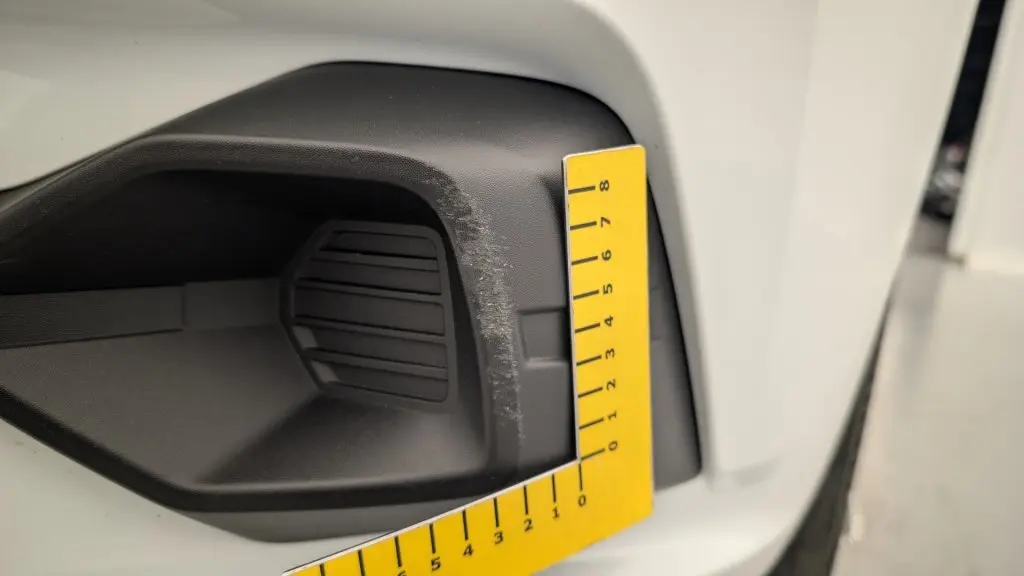 Gros plan sur l'entrée d'air avant droite noire avec rayures sur la carrosserie blanche d'une Dacia Sandero 2022.