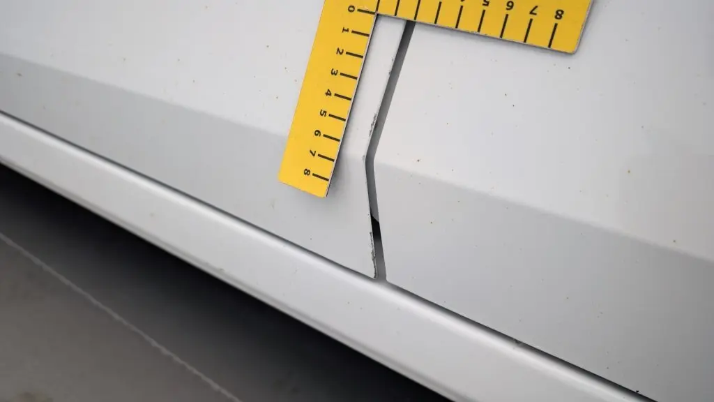 Détail de la portière blanche de la Dacia Sandero 2022 avec un écart anormal et un outil de mesure jaune posé dessus.