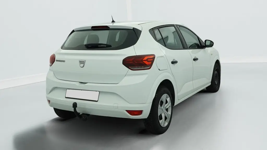 Vue 3/4 arrière droite d'une Dacia Sandero blanche avec feux arrière LED et attelage de remorque visible.