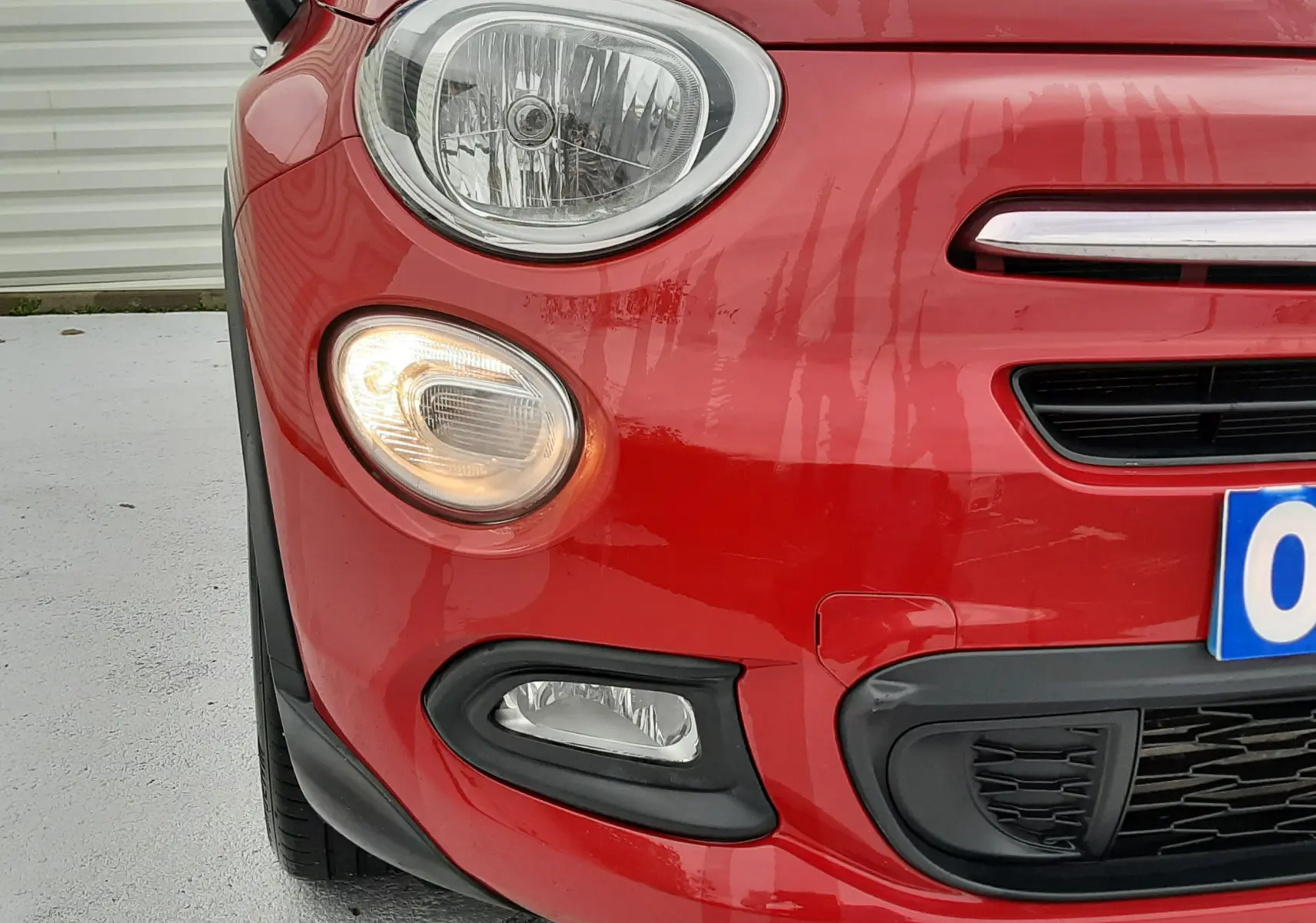 Gros plan sur l'avant gauche rouge vif du Fiat 500X 2016, avec phare et clignotant allumé visible.