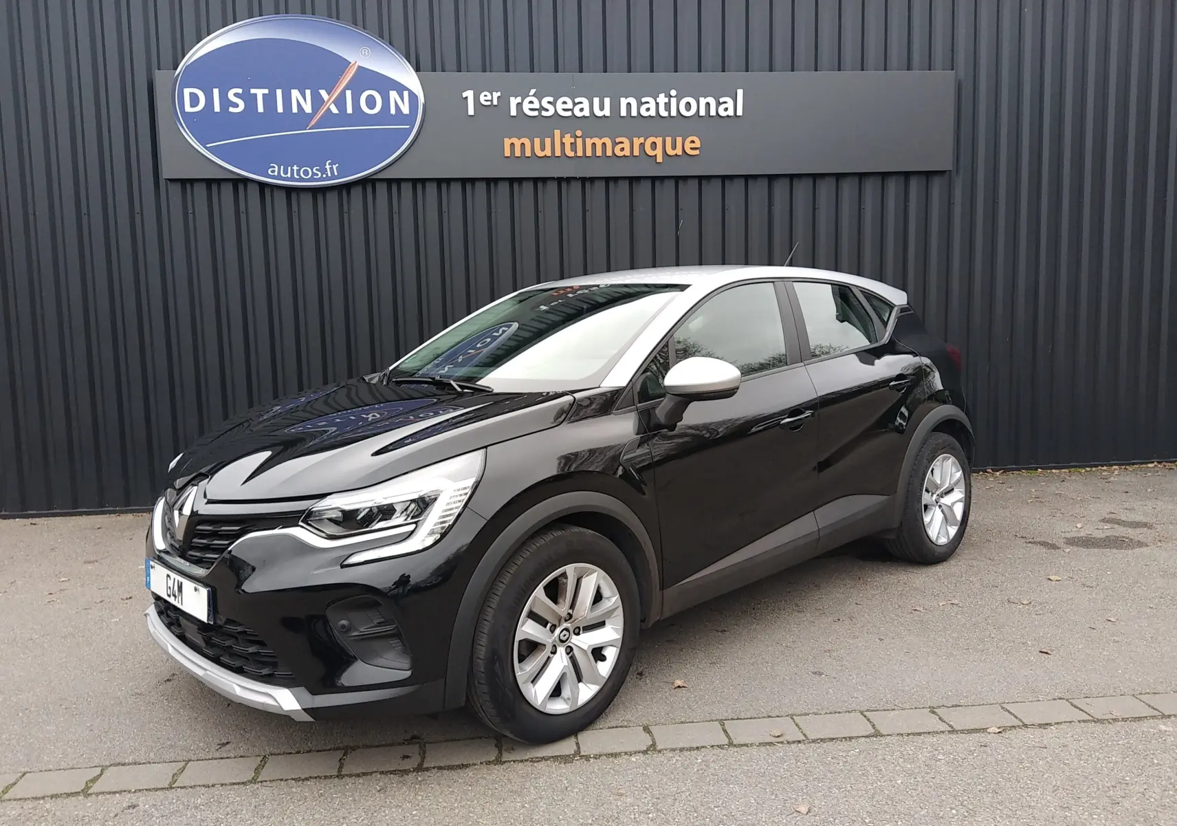 Renault Captur noir 3/4 avant droit avec toit blanc, stationné devant un mur noir avec enseigne Distinxion.