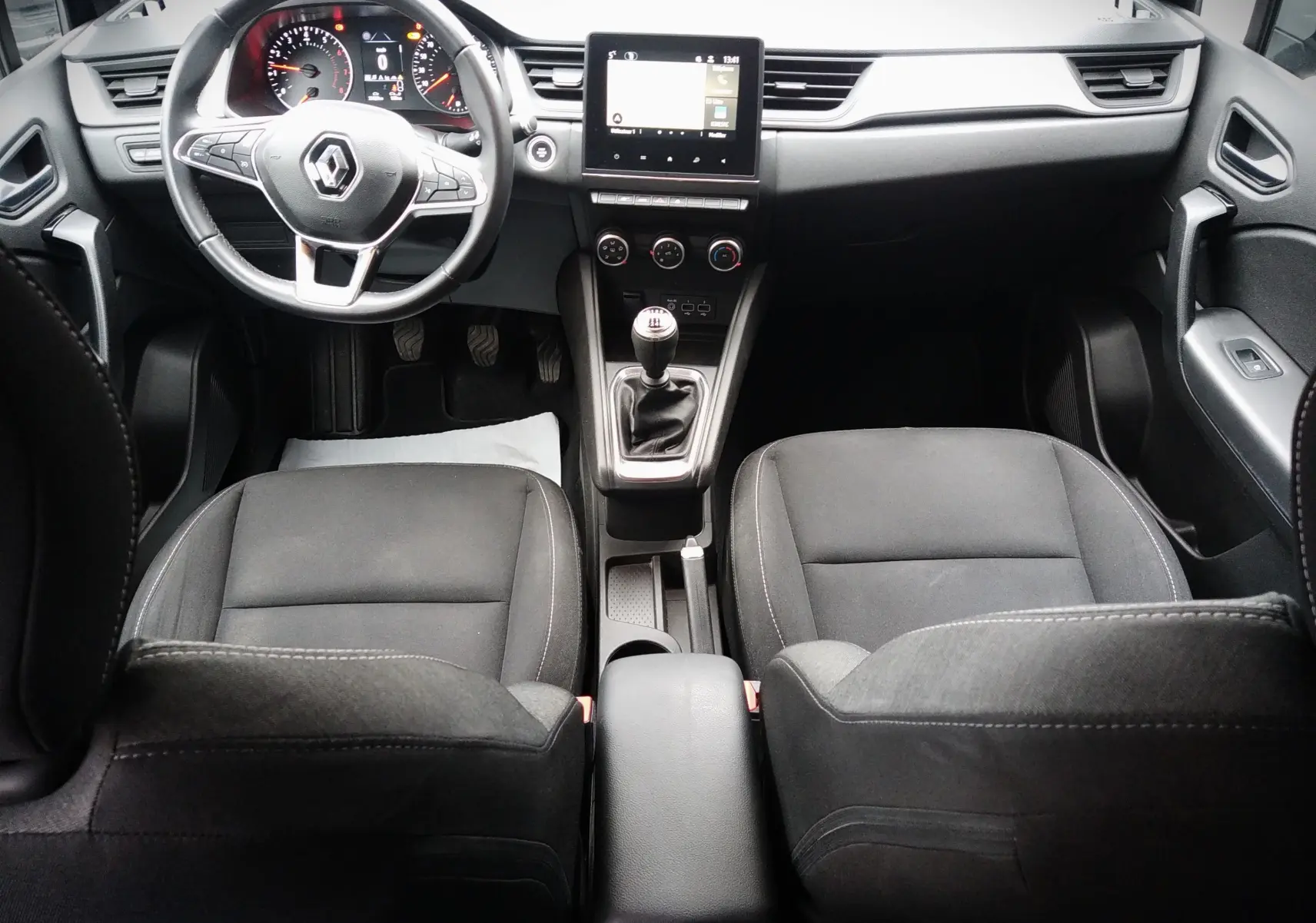 Vue intérieure avant du Renault Captur noir 2021, mettant en valeur le volant, la console centrale avec boîte manuelle et l'écran tactile.