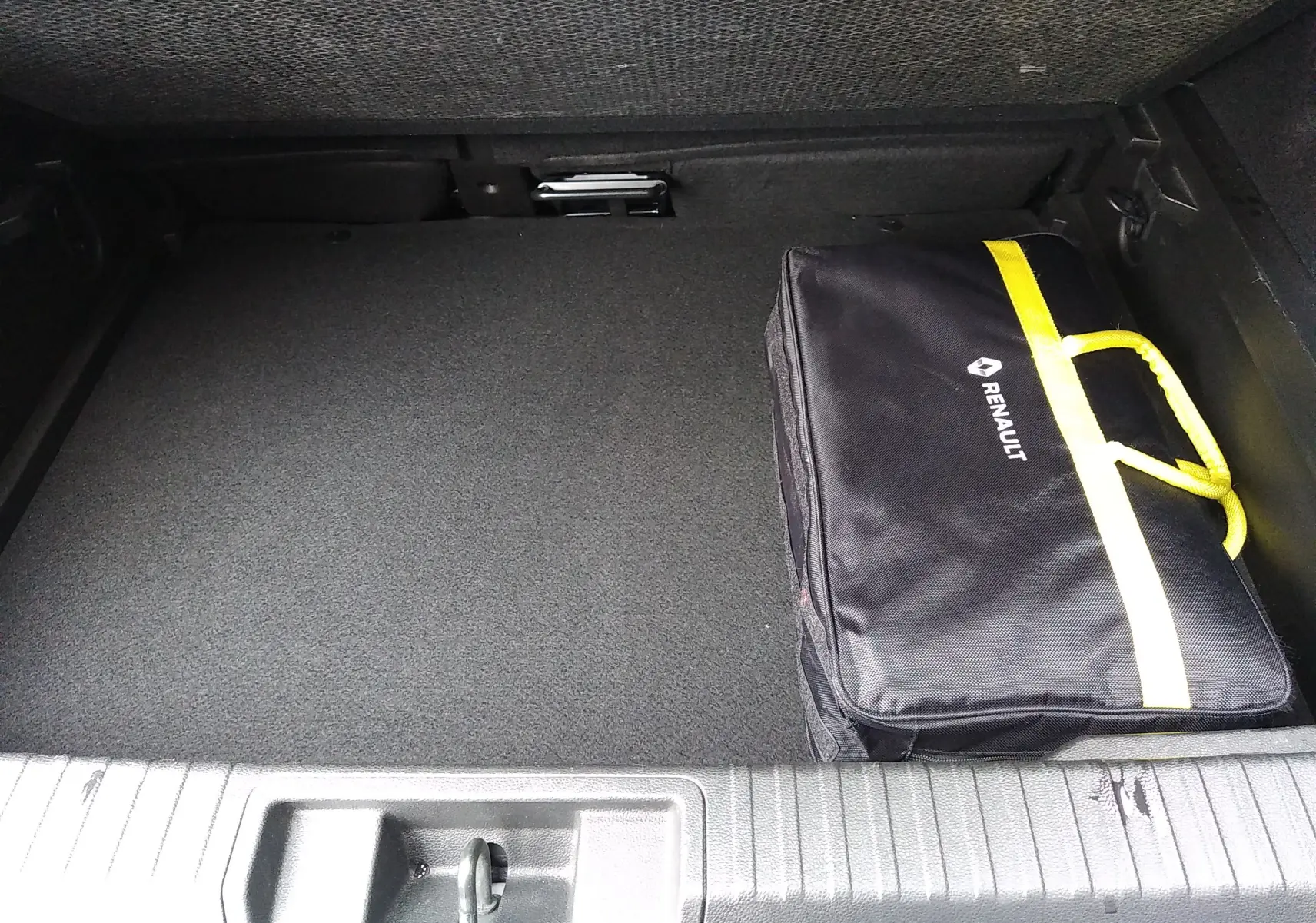 Coffre ouvert d’un Renault Captur noir 2021, vue plongeante montrant un sac de secours noir avec une bande jaune.