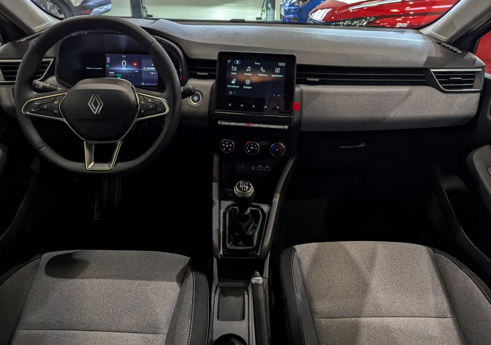 Vue intérieure avant de la Renault Clio V Gris Rafale, montrant le volant, tableau de bord digital et la console centrale avec boîte manuelle.