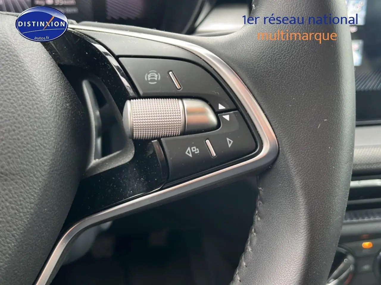 Gros plan sur les commandes gauche du volant cuir noir de la Skoda Fabia blanche, avec détails chromés et boutons multifonctions.