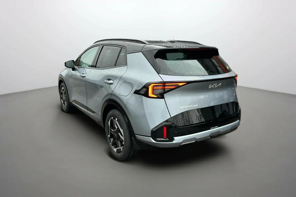 Vue 3/4 arrière droite d'un Kia Sportage gris perle avec toit noir et feux arrière LED allumés.
