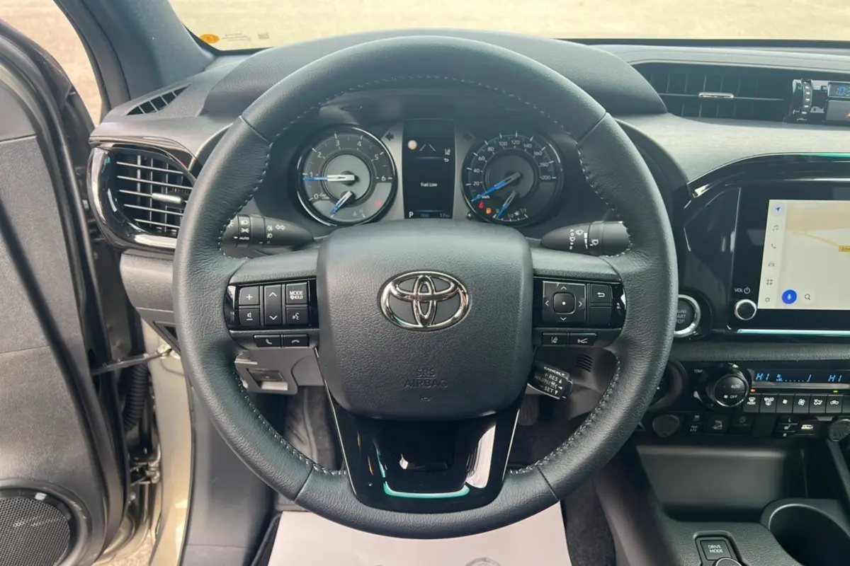 Vue intérieure centrée sur le volant du Toyota Hilux 2025, avec tableau de bord et écran tactile visibles.