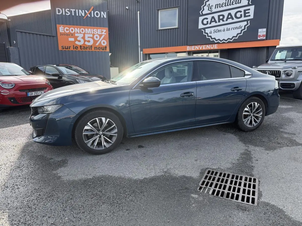 Peugeot 508 bleu métallisé vue de profil côté gauche, avec jantes alliage et vitres surteintées, stationnée devant un garage.