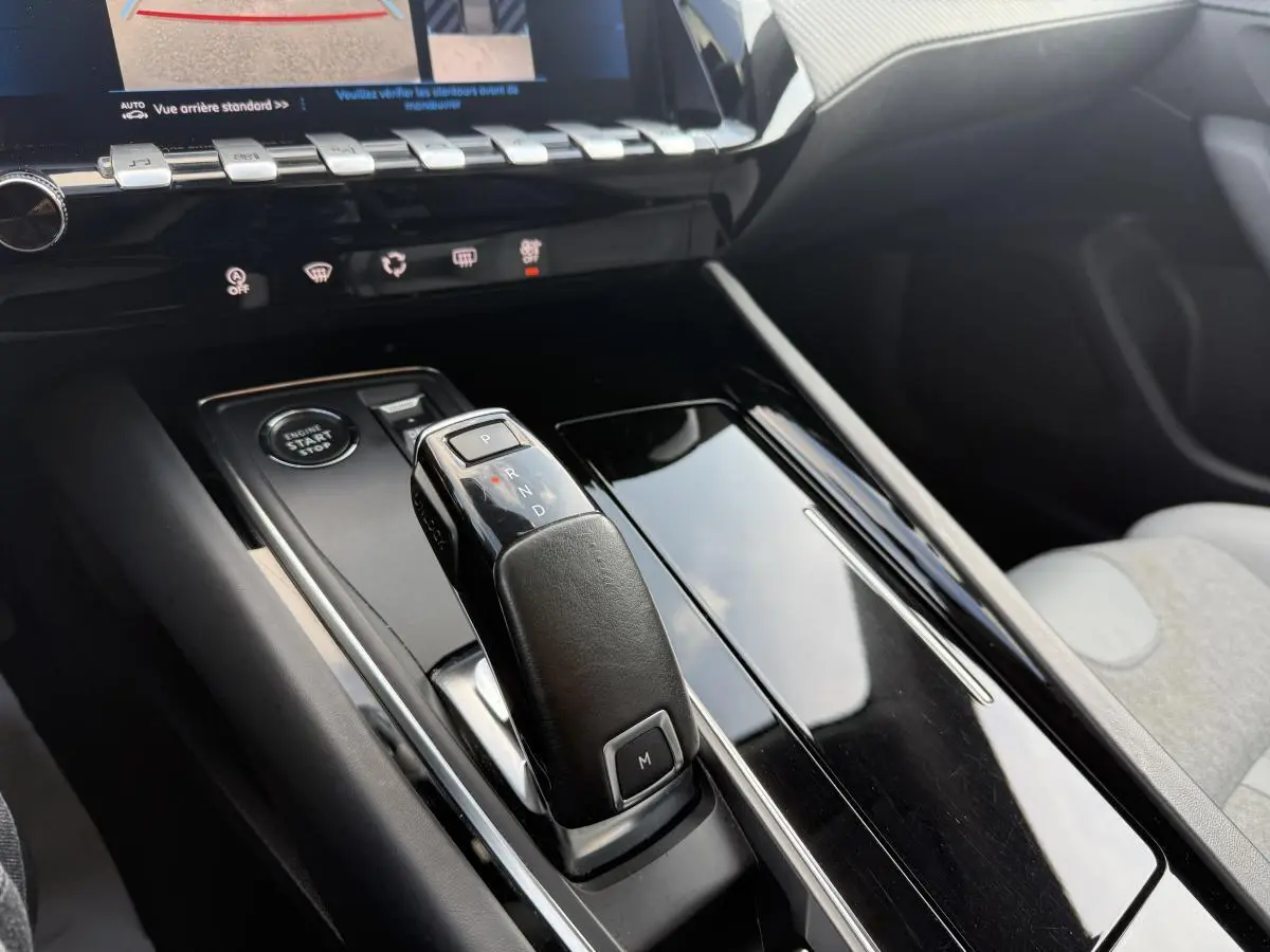 Gros plan sur la console centrale noire brillante de la Peugeot 508 bleu, avec levier de boîte automatique et bouton start/stop.
