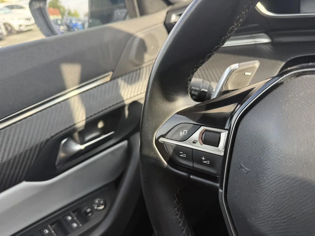 Détail du volant et de la porte côté conducteur avec décor carbone et commandes intégrées sur Peugeot 508 bleu.