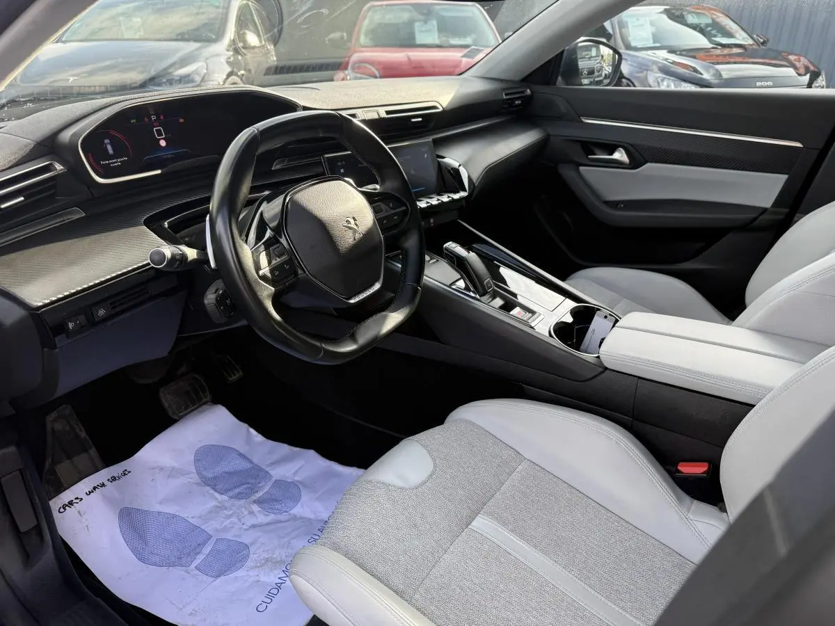 Vue intérieure côté conducteur du Peugeot 508 2019, avec sellerie gris clair et tableau de bord noir à inserts carbone.