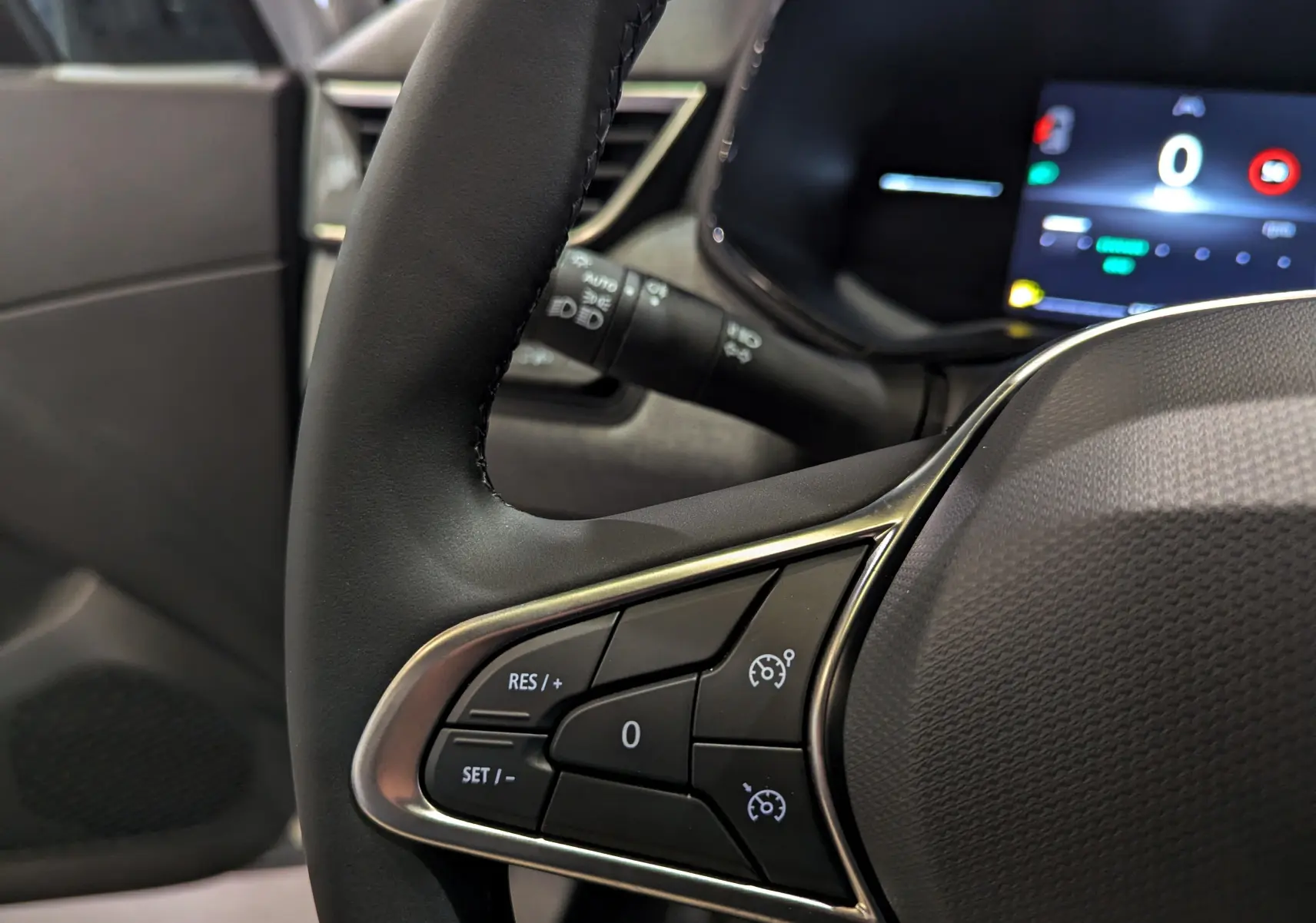 Gros plan sur le volant noir de la Renault Clio V avec commandes de régulateur de vitesse et tableau de bord numérique en arrière-plan.