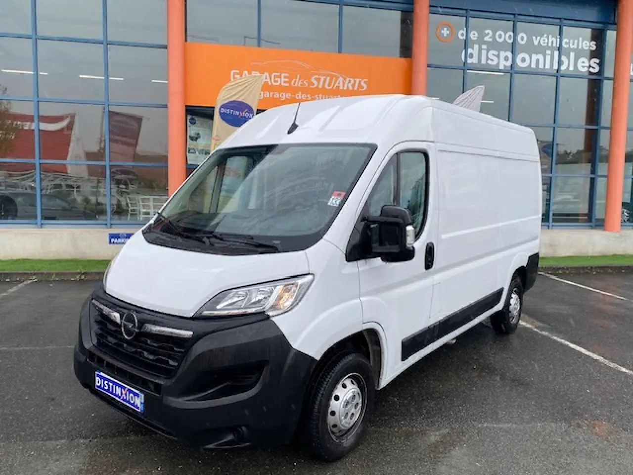 Vue 3/4 avant droit d’un Opel Movano Fourgon blanc avec porte latérale coulissante et pare-chocs noir, stationné devant un garage.