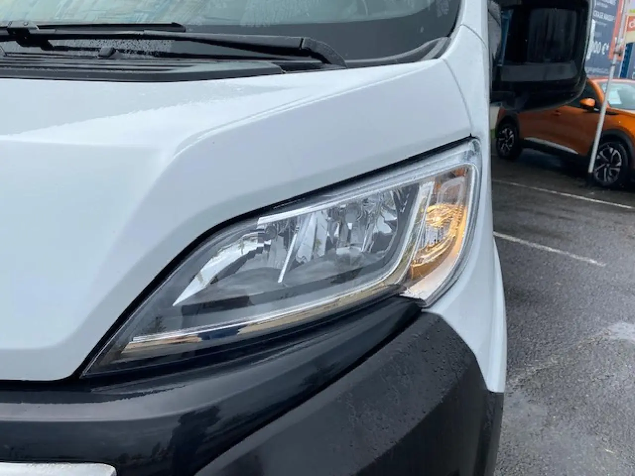 Gros plan sur le phare avant droit du fourgon blanc Opel Movano 2023, avec pare-chocs noir et rétroviseur visible.