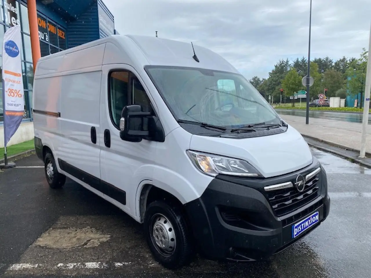 Vue 3/4 avant droit d’un Opel Movano Fourgon blanc avec porte latérale coulissante, stationné sous un ciel couvert.