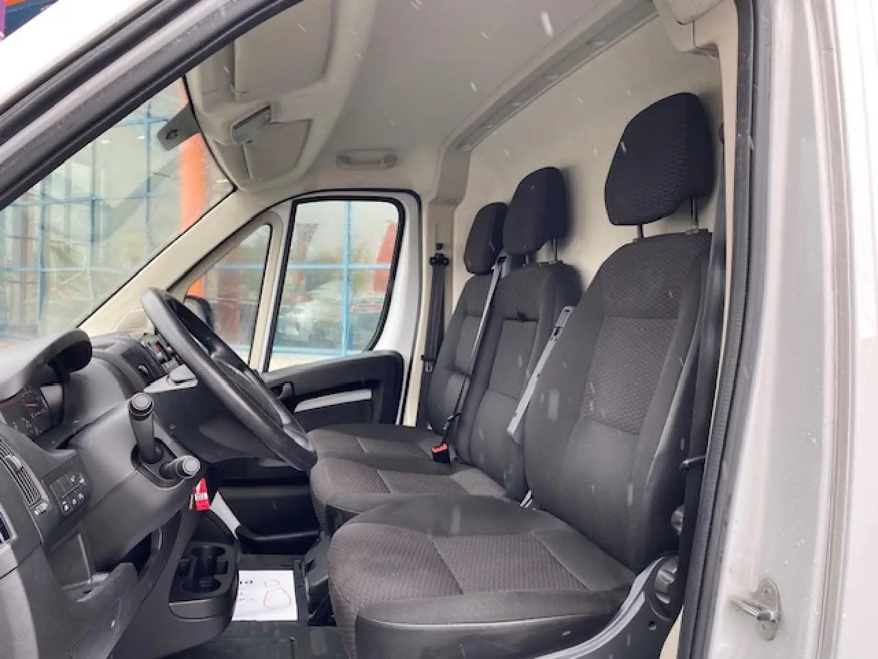 Vue intérieure côté conducteur de l'Opel Movano Fourgon blanc, montrant la banquette 3 places et le volant.