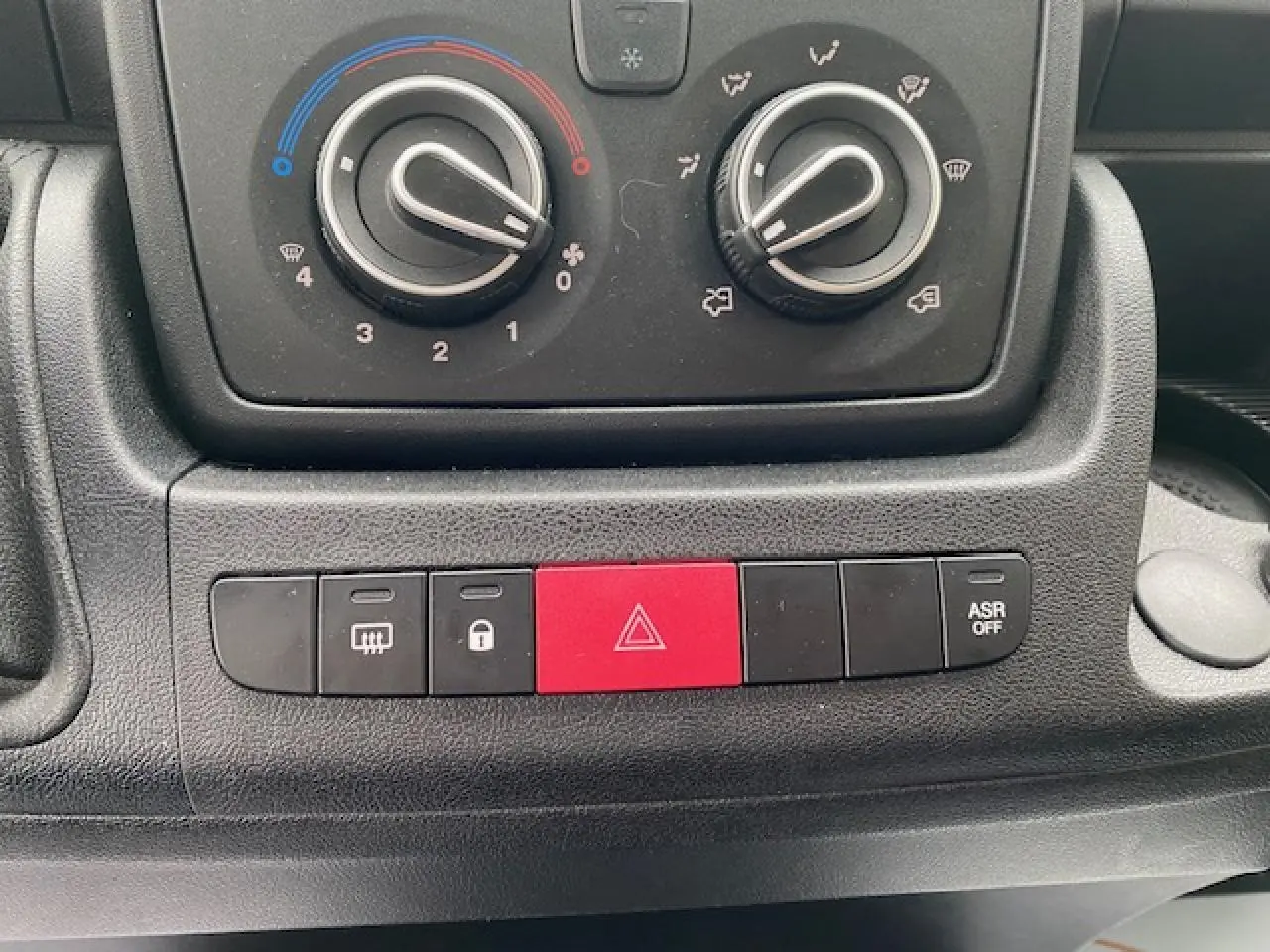 Gros plan sur les commandes de climatisation et les boutons de sécurité du tableau de bord noir de l’Opel Movano Fourgon 2023.