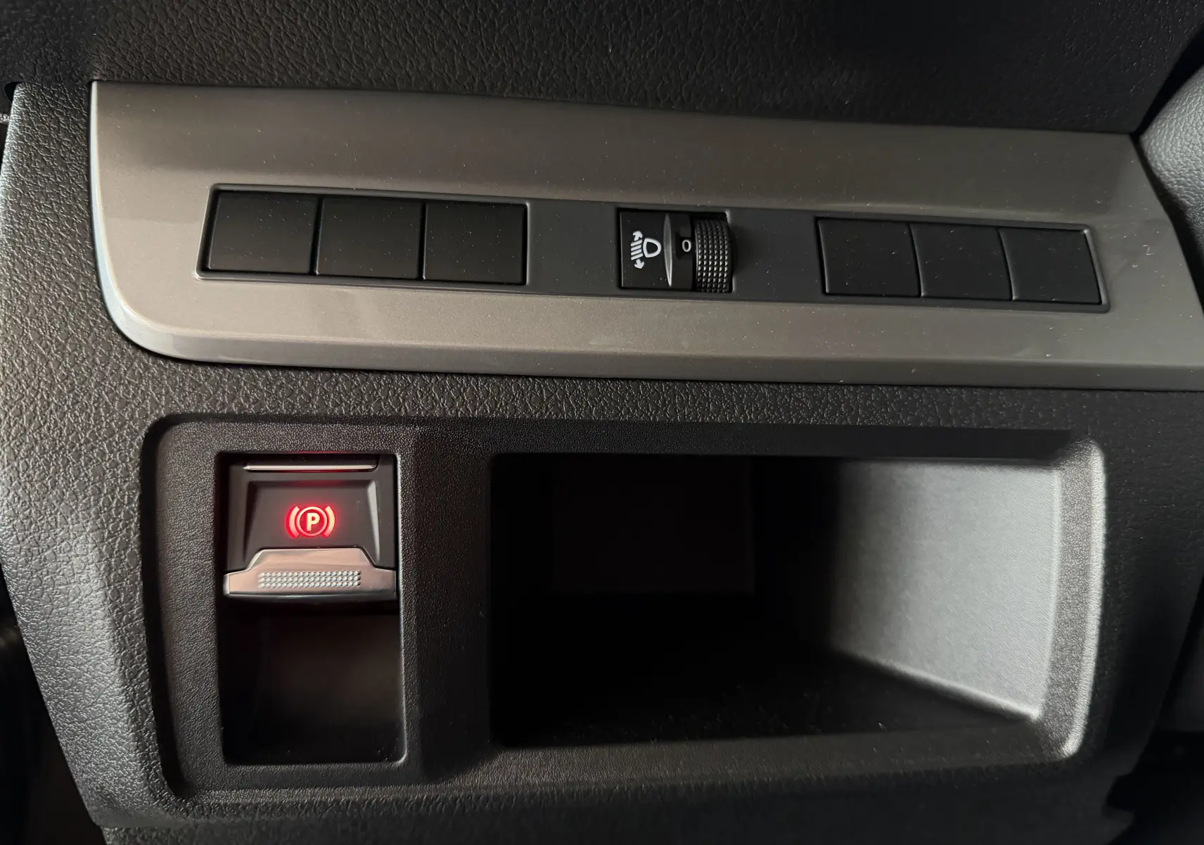 Gros plan sur la commande de frein à main électrique rouge et le réglage des phares sur le tableau de bord noir du Citroën Jumpy Gris Titane.