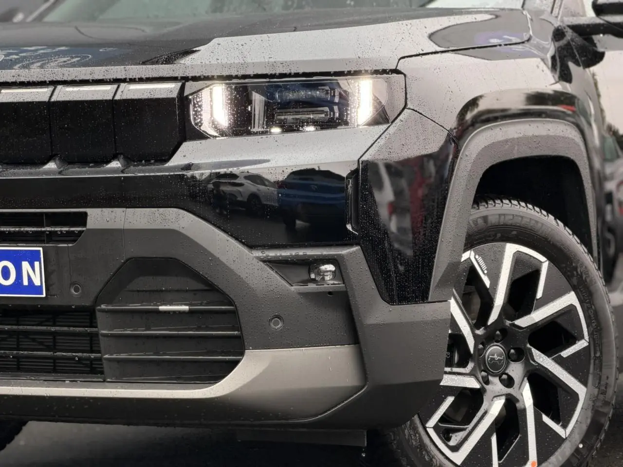 Gros plan sur l'avant droit noir Vulcano du Jeep Compass Hybrid 145 e-DSC6 avec jante alliage 19 pouces et phares LED allumés.
