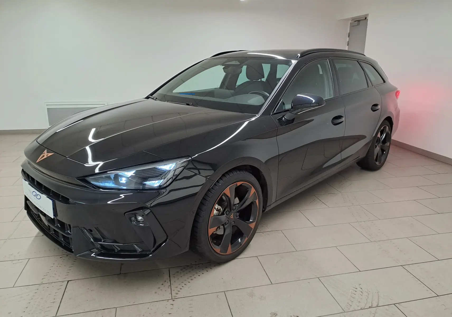 Vue 3/4 avant droite d'une CUPRA Leon ST 2025 noir minuit avec jantes alliage 18'' cuivrées et phares LED allumés.