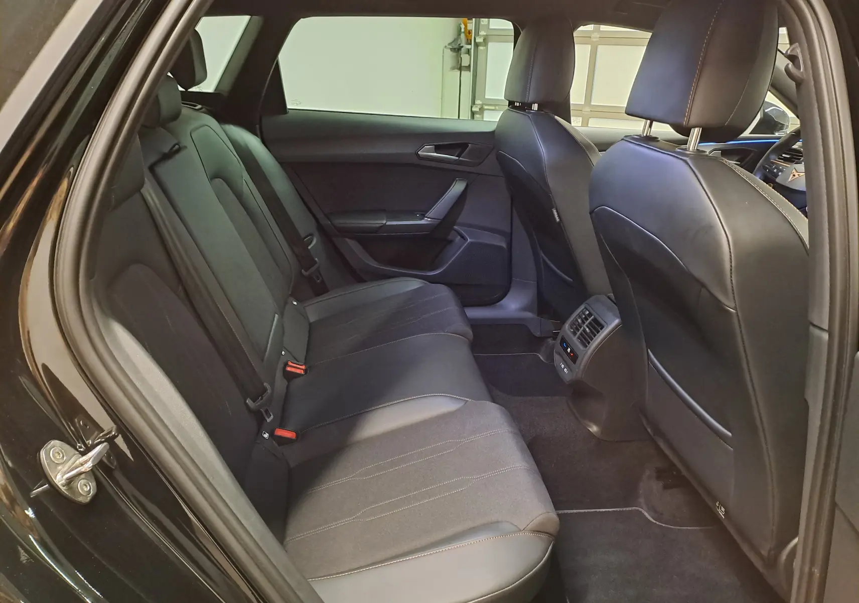 Vue intérieure arrière côté gauche du CUPRA LEON ST 1.5 eTSI 150 DSG7 noir minuit avec sièges en cuir et tissu.