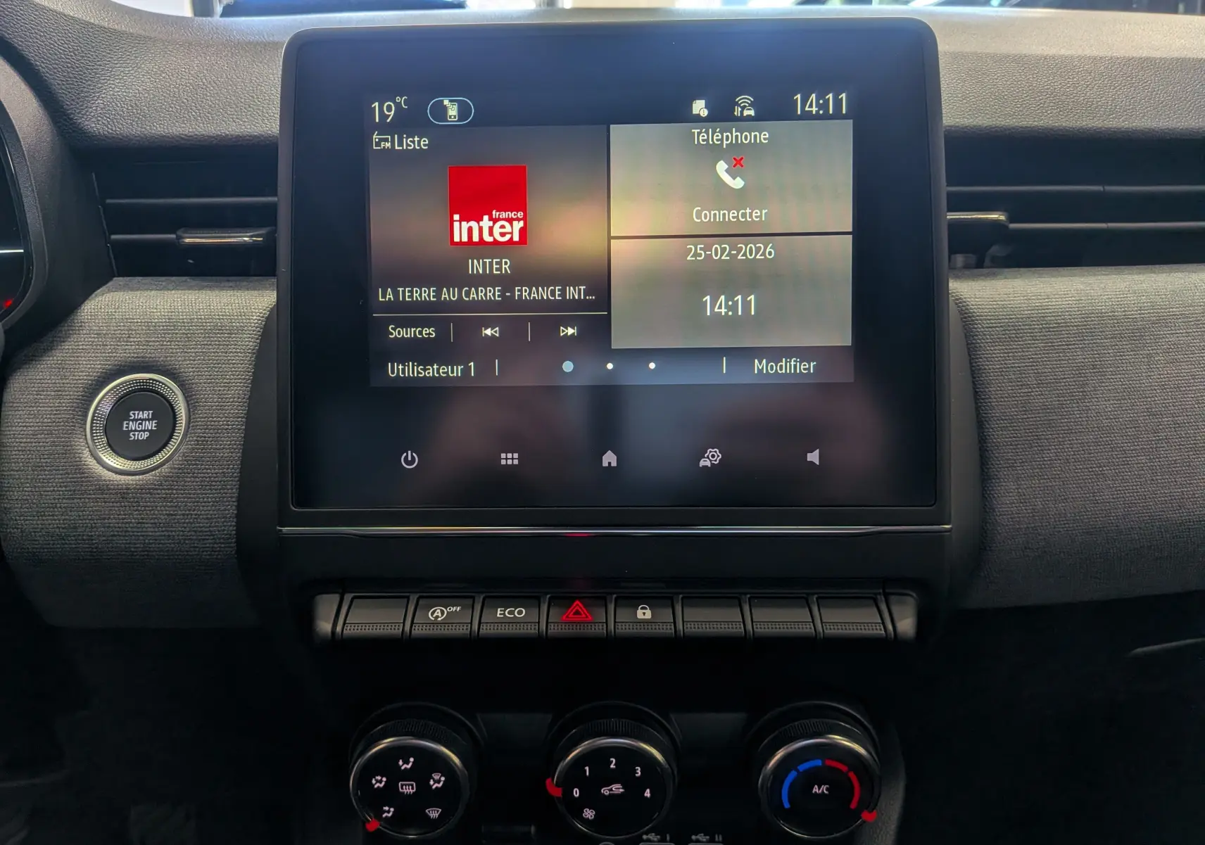 Vue rapprochée de l’écran tactile central et des commandes de climatisation de la Renault Clio V Bleu Iron, intérieur noir.