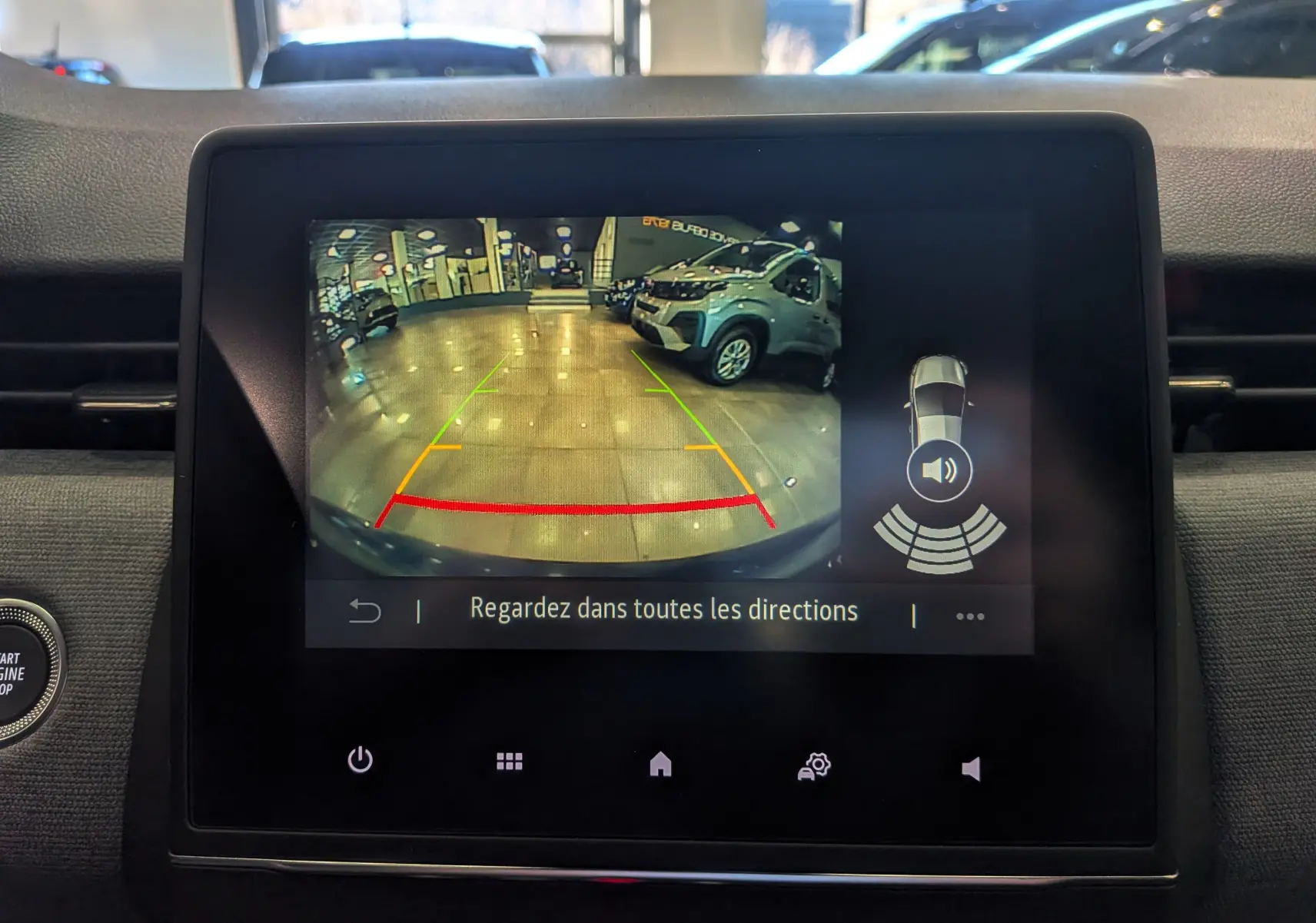 Écran multimédia montrant la caméra de recul avec vue arrière d’un véhicule blanc dans un garage lumineux.