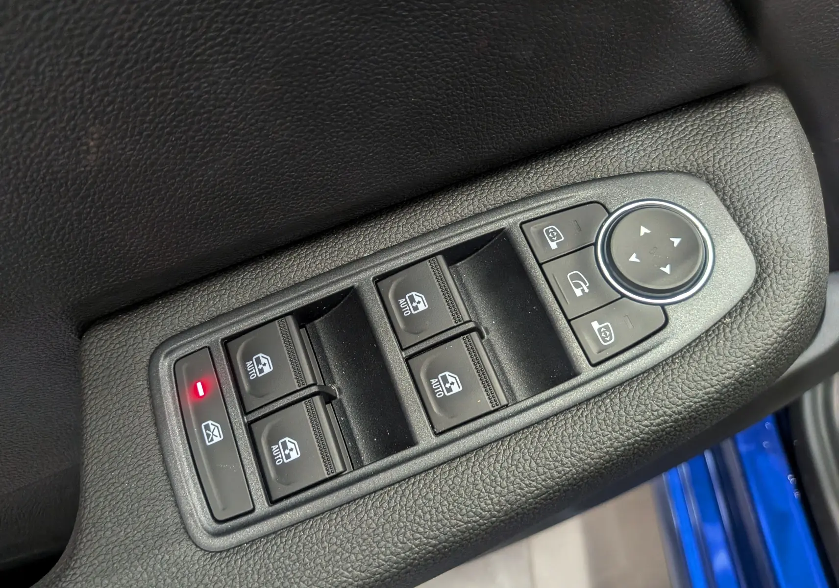 Gros plan sur les commandes des vitres électriques et rétroviseurs côté conducteur, avec bordure de porte bleu Iron visible.