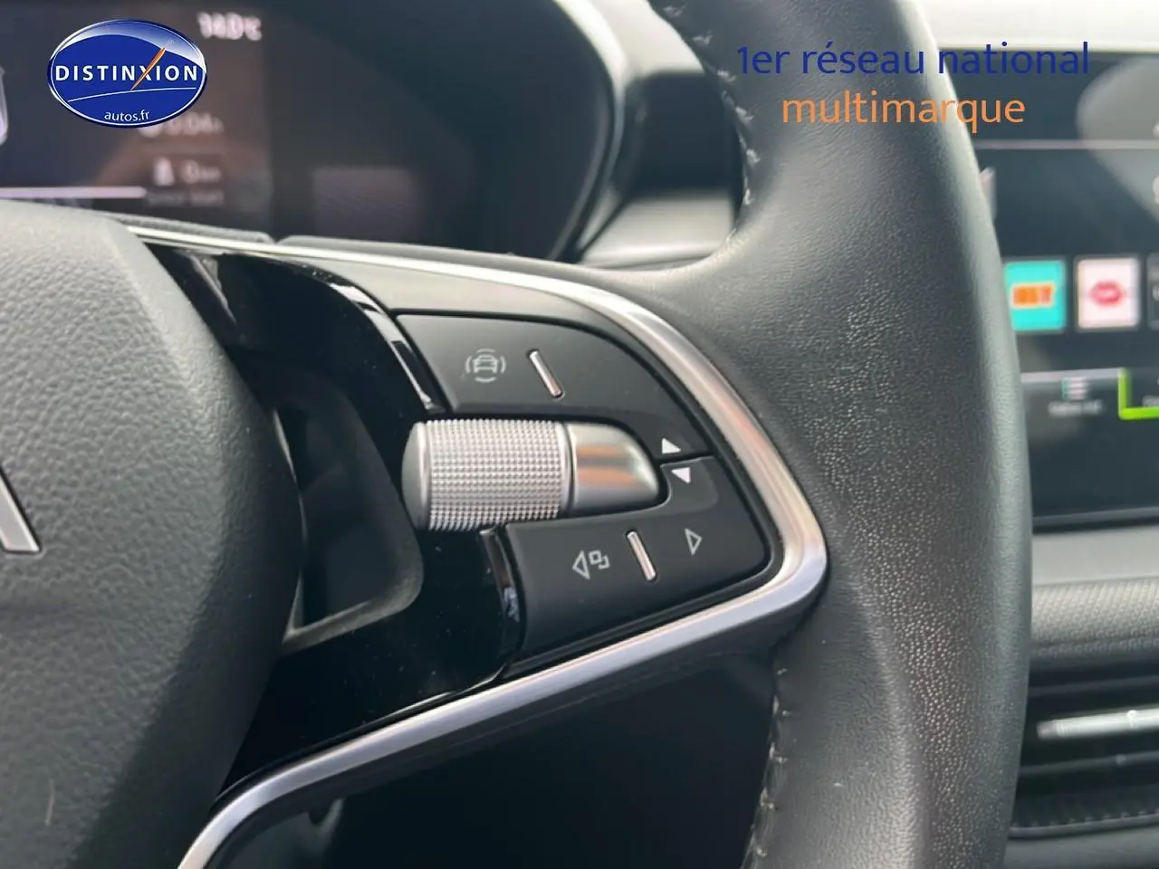 Gros plan sur les commandes multifonctions à gauche du volant cuir d'une Skoda Fabia bleu, avec écran tactile en arrière-plan.