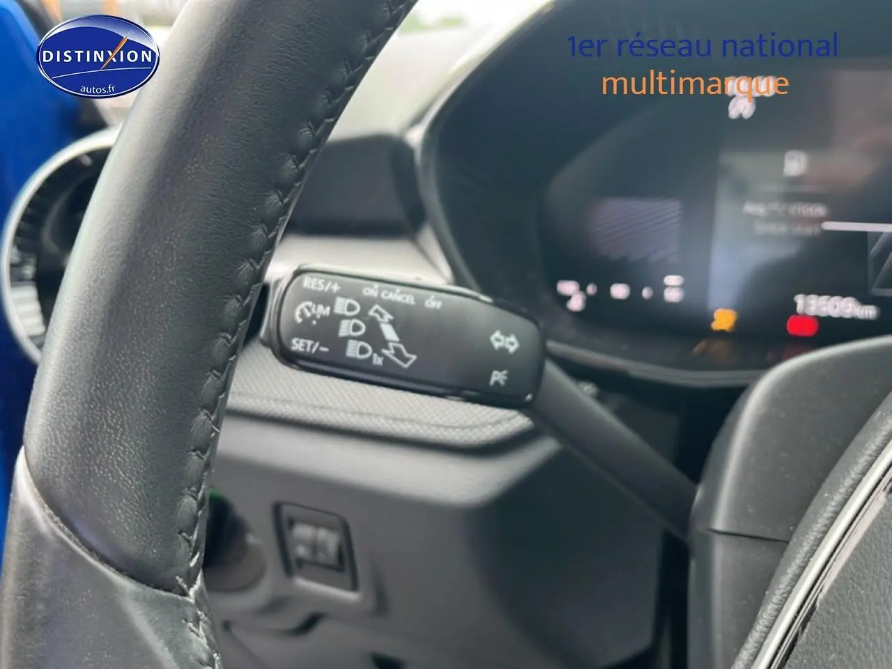 Gros plan sur le volant cuir noir et la commande de clignotant d'une Skoda Fabia bleue, tableau de bord numérique en arrière-plan flou.