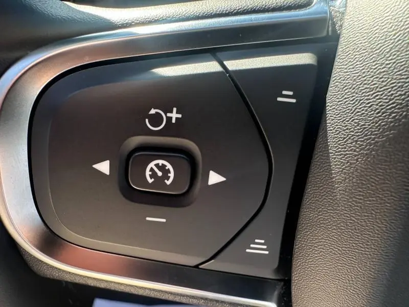 Gros plan sur les commandes de régulateur de vitesse au volant noir du Volvo S60 B4 2024 gris Platinium métallisé.