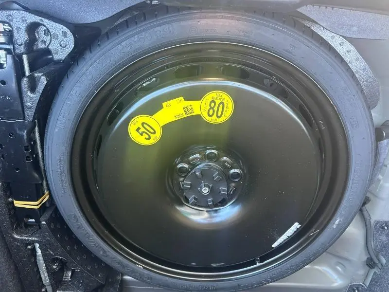 Gros plan sur la roue de secours noire avec étiquettes jaunes de limitation de vitesse, dans le coffre d'une Volvo S60 gris Platinium.