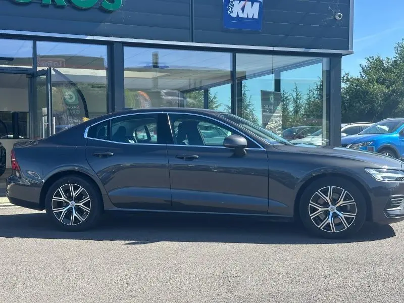 Vue de profil côté gauche d'une Volvo S60 B4 gris Platinium métallisé, avec jantes alliage et poignées ton carrosserie.