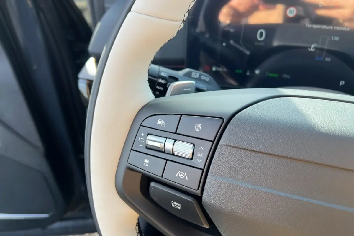 Gros plan sur le volant cuir beige et noir du Kia Sportage 2026, avec commandes multifonctions côté gauche et tableau de bord numérique.