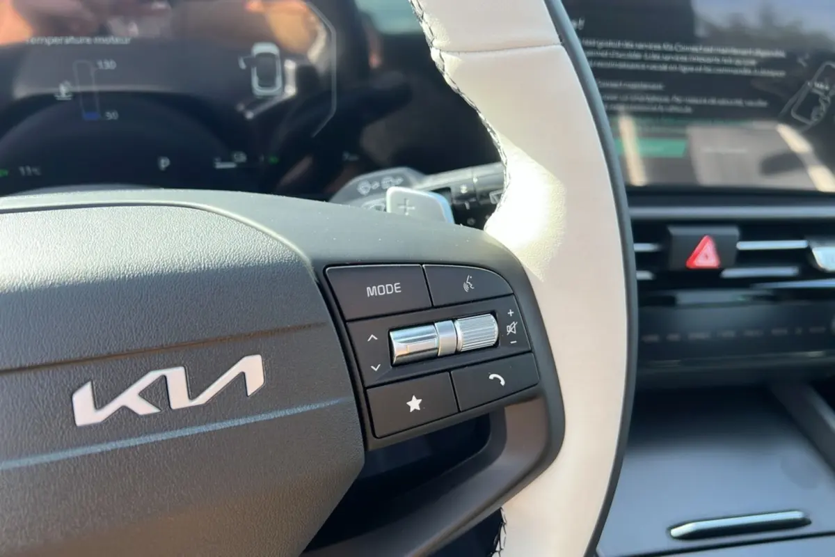 Gros plan sur le volant cuir blanc et noir du Kia Sportage 2026 avec commandes multifonctions et tableau de bord numérique flou.