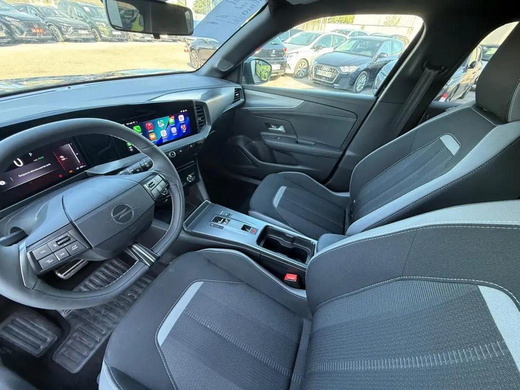 Vue intérieure côté conducteur de l’Opel Mokka électrique 2025, montrant le volant, écran tactile et sièges noirs avec surpiqûres grises.