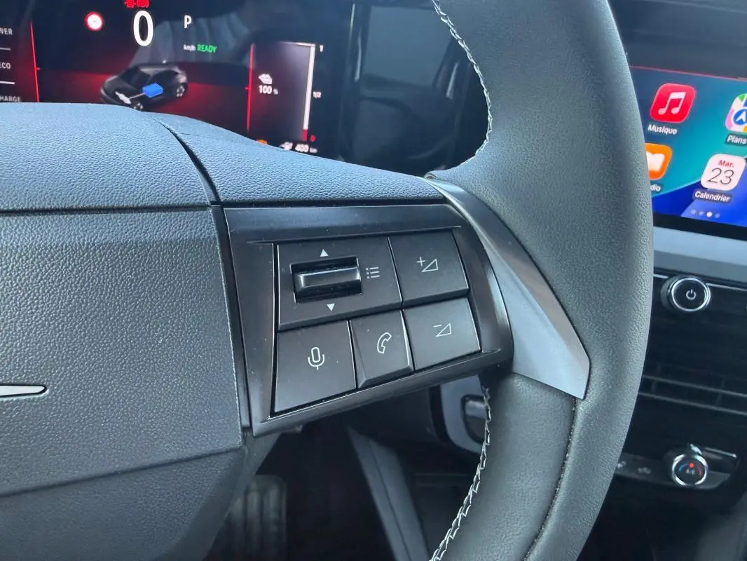 Gros plan sur les commandes au volant côté gauche de l’Opel Mokka électrique 2025, avec écran tactile en arrière-plan.