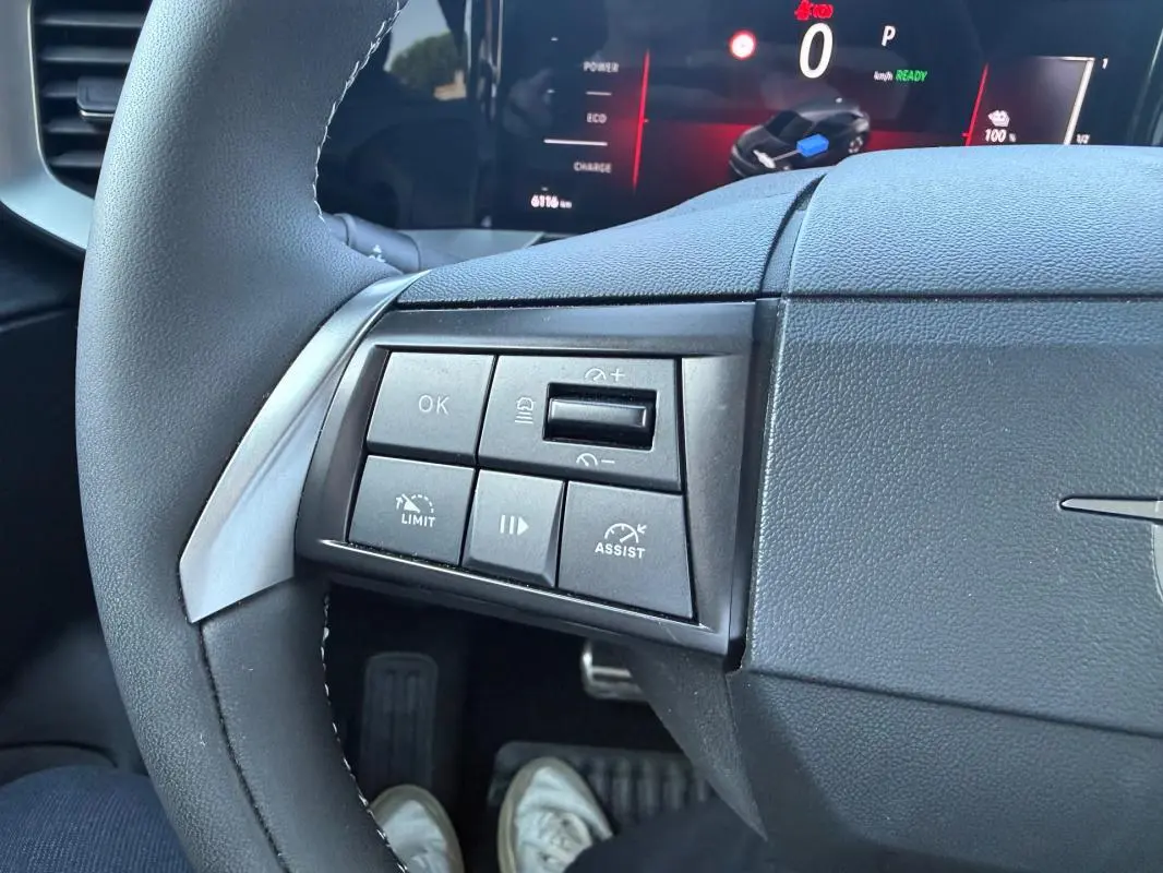 Gros plan sur les commandes à gauche du volant noir de l’Opel Mokka électrique 2025 avec écran numérique en arrière-plan.