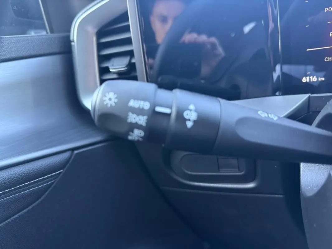 Gros plan sur la commande des phares à gauche du volant dans l'habitacle noir de l'Opel Mokka électrique 2025.