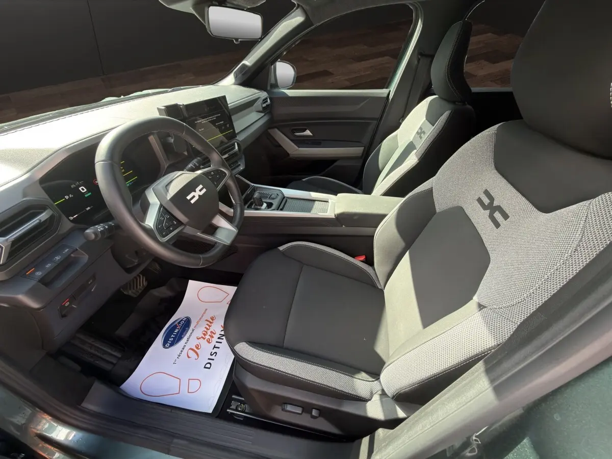 Vue intérieure côté conducteur du Dacia Bigster Journey hybride vert 2025, avec sièges tissu bicolore et volant multifonctions.
