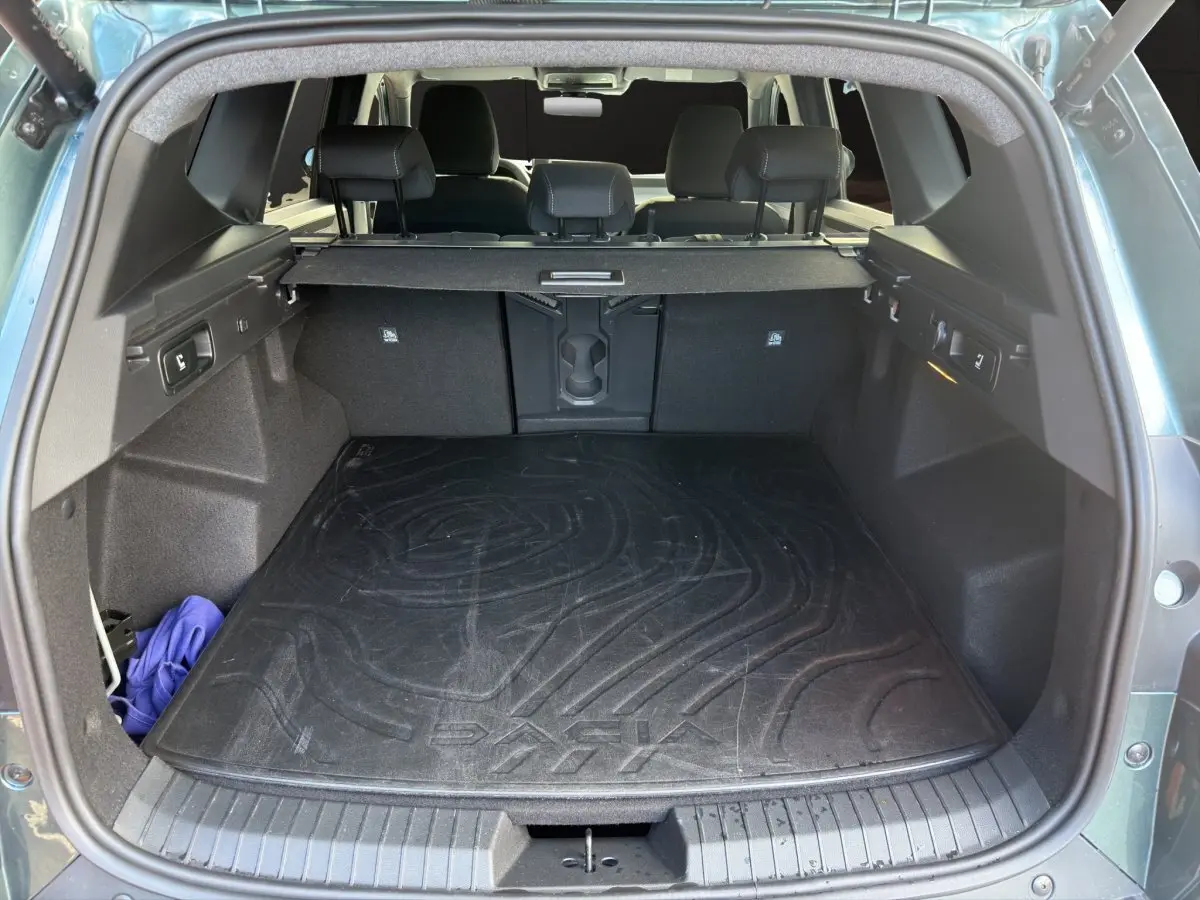 Coffre ouvert d'un Dacia Bigster vert, vue arrière montrant la grande capacité et le tapis de coffre noir marqué Dacia.