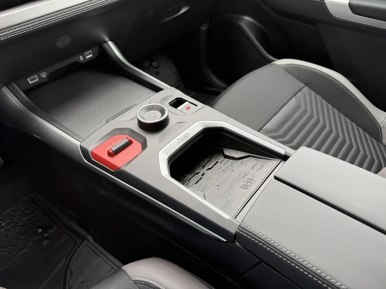 Gros plan sur la console centrale intérieure du Jeep Compass 2026, avec sellerie mixte gris et chargeur sans fil visible.