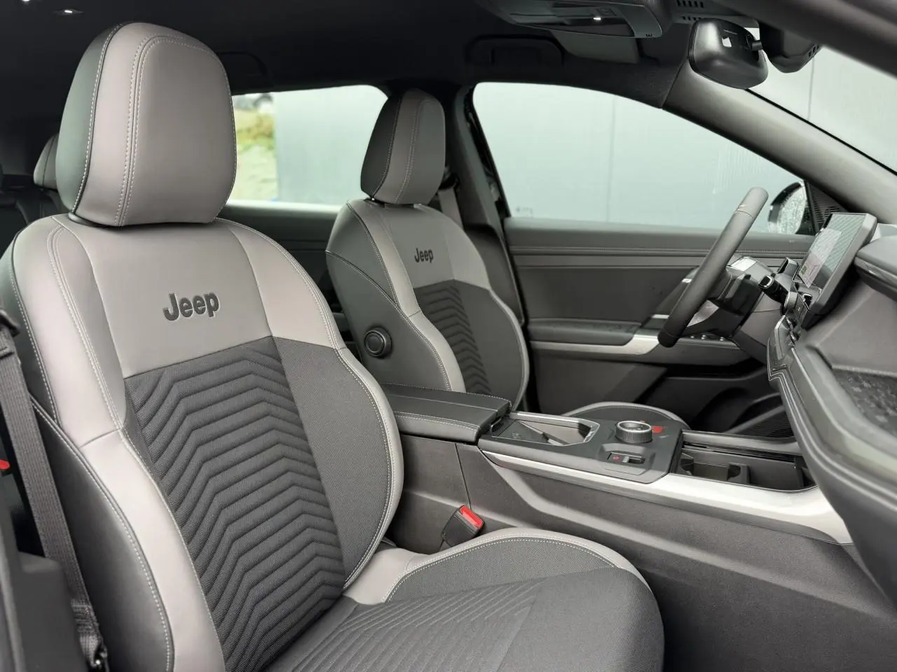Vue intérieure côté conducteur du Jeep Compass 2026, sellerie mixte gris anthracite avec logo Jeep brodé sur les sièges.