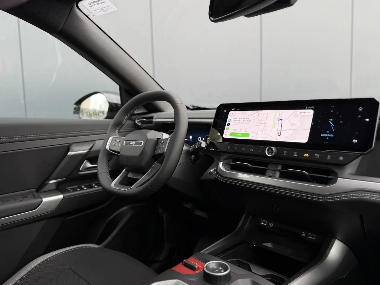 Intérieur du Jeep Compass 2026 vu côté conducteur, tableau de bord noir avec écran tactile large affichant la navigation.