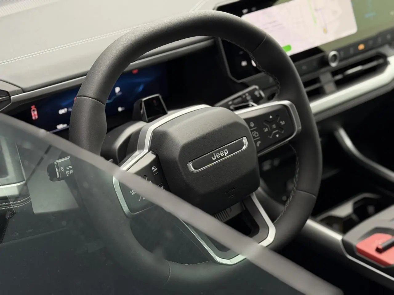 Vue rapprochée du volant noir du Jeep Compass 2026 avec tableau de bord numérique et écran tactile visible en arrière-plan.