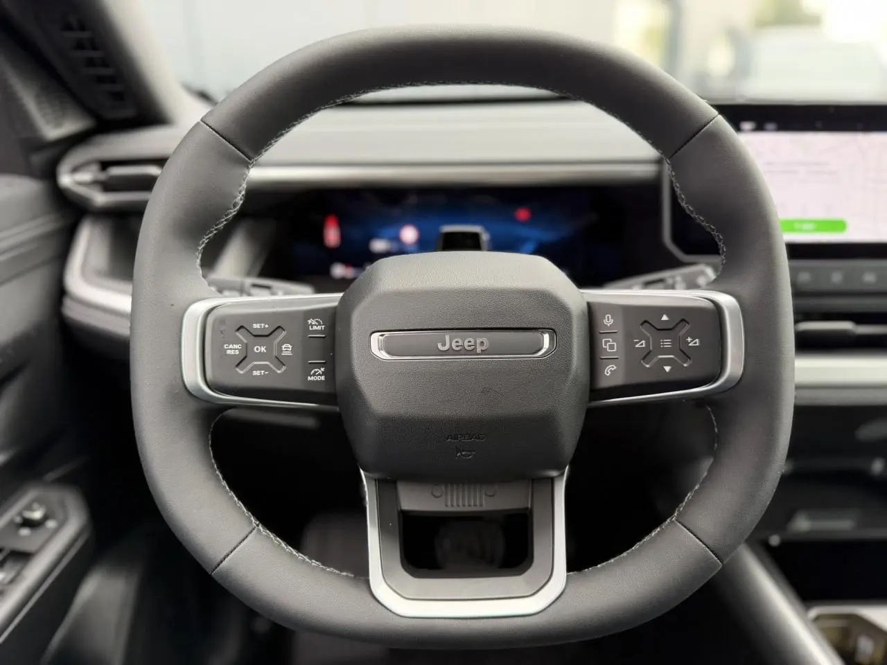 Vue rapprochée du volant noir du Jeep Compass 2026 avec commandes intégrées et tableau de bord numérique flou.