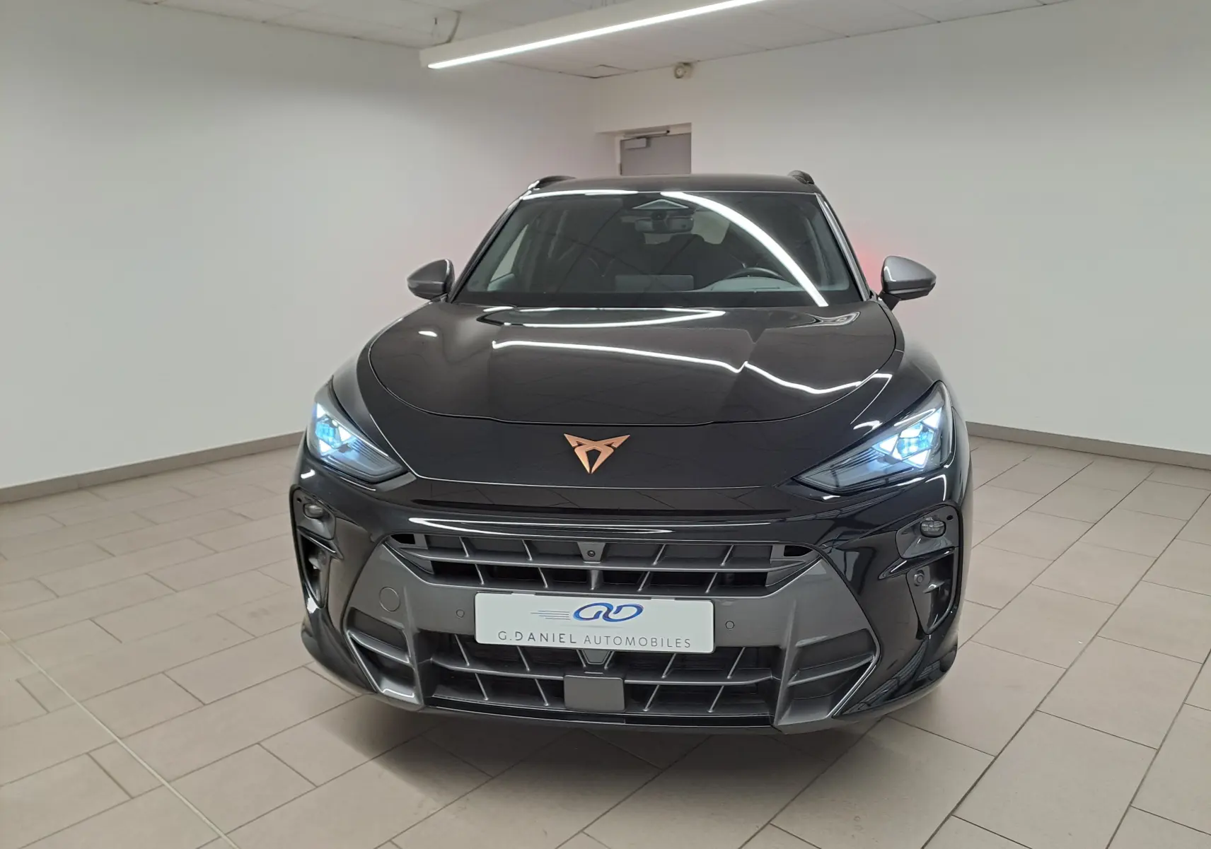 Vue avant d'une CUPRA TERRAMAR 2025 noir minuit avec feux allumés et logo cuivré dans un showroom.
