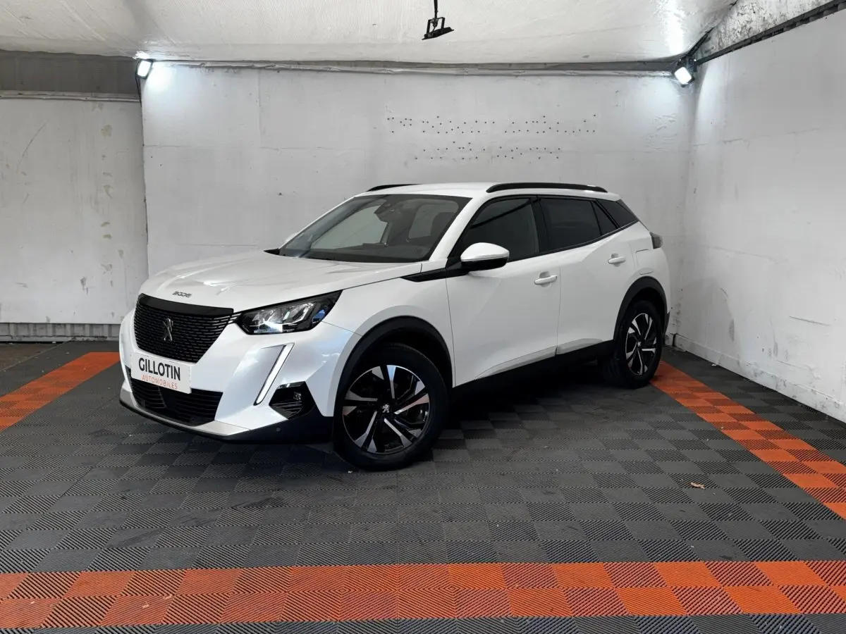 Peugeot 2008 blanc en 3/4 avant droit, avec jantes noires et toit noir dans un garage éclairé.