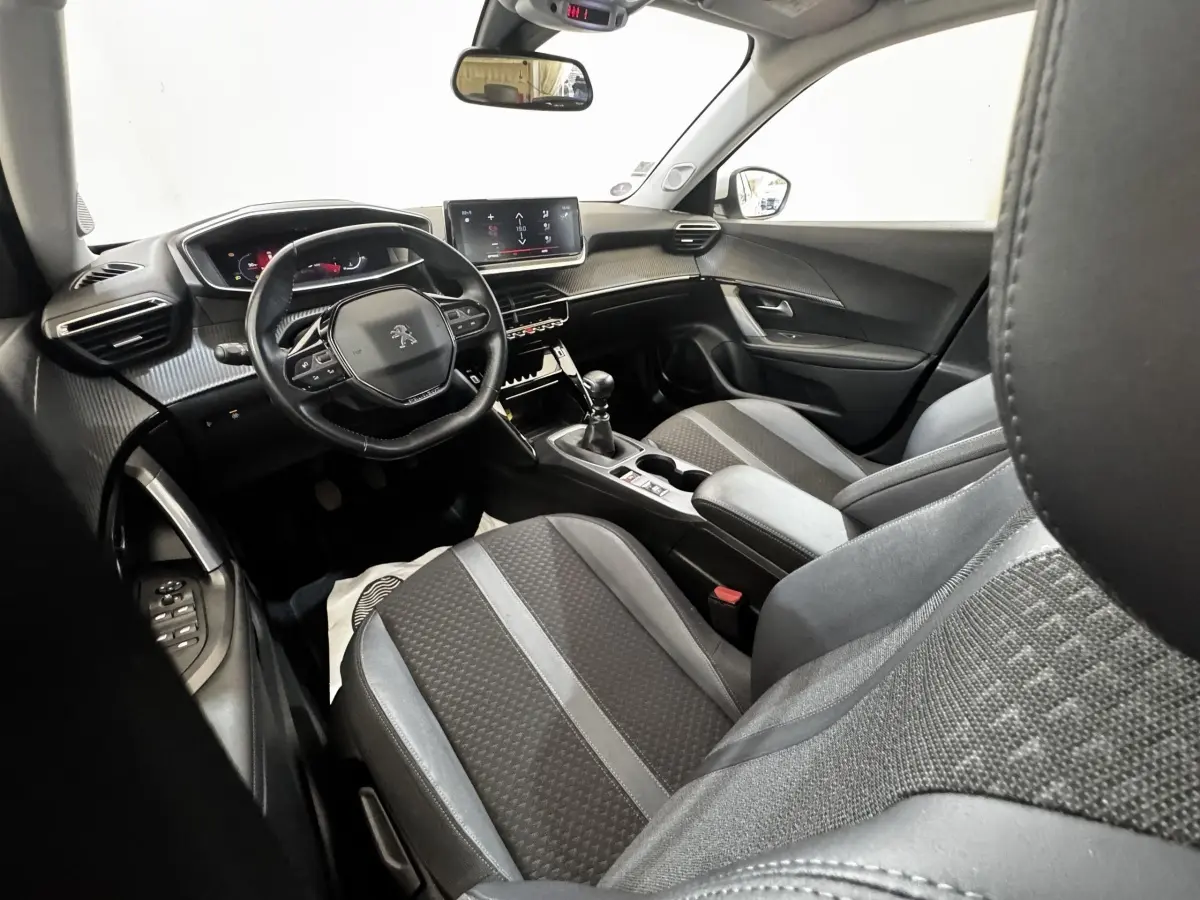 Intérieur de la Peugeot 2008 blanc, vue côté conducteur, volant cuir multifonctions et écran tactile central visible.
