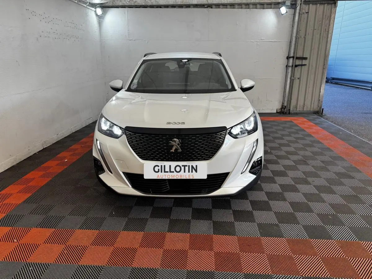 Peugeot 2008 blanc vue de face en intérieur, avec calandre noire et phares LED allumés.